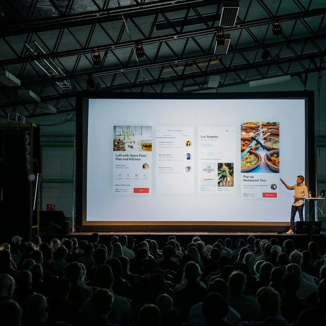 person discussing while standing in front of a large screen in front of people inside dim-lighted room